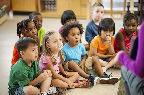 Enfants de divers origines assis, écoutant attentivement leur professeur